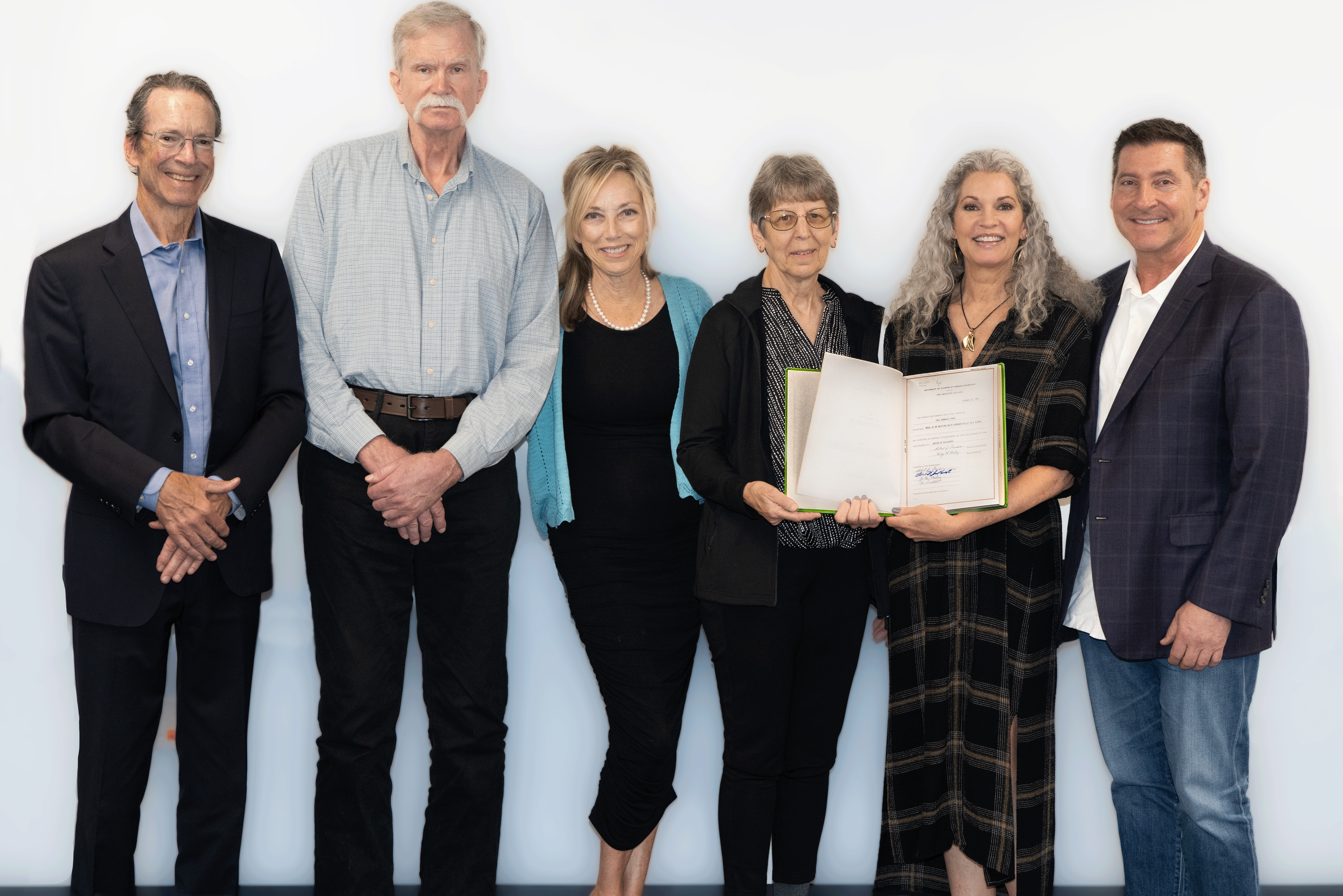 Family members of estate donor pose for a photo, holding his dissertation.