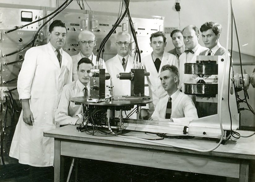 A group of men in lab coats standing in front of a machineAI-generated content may be incorrect.