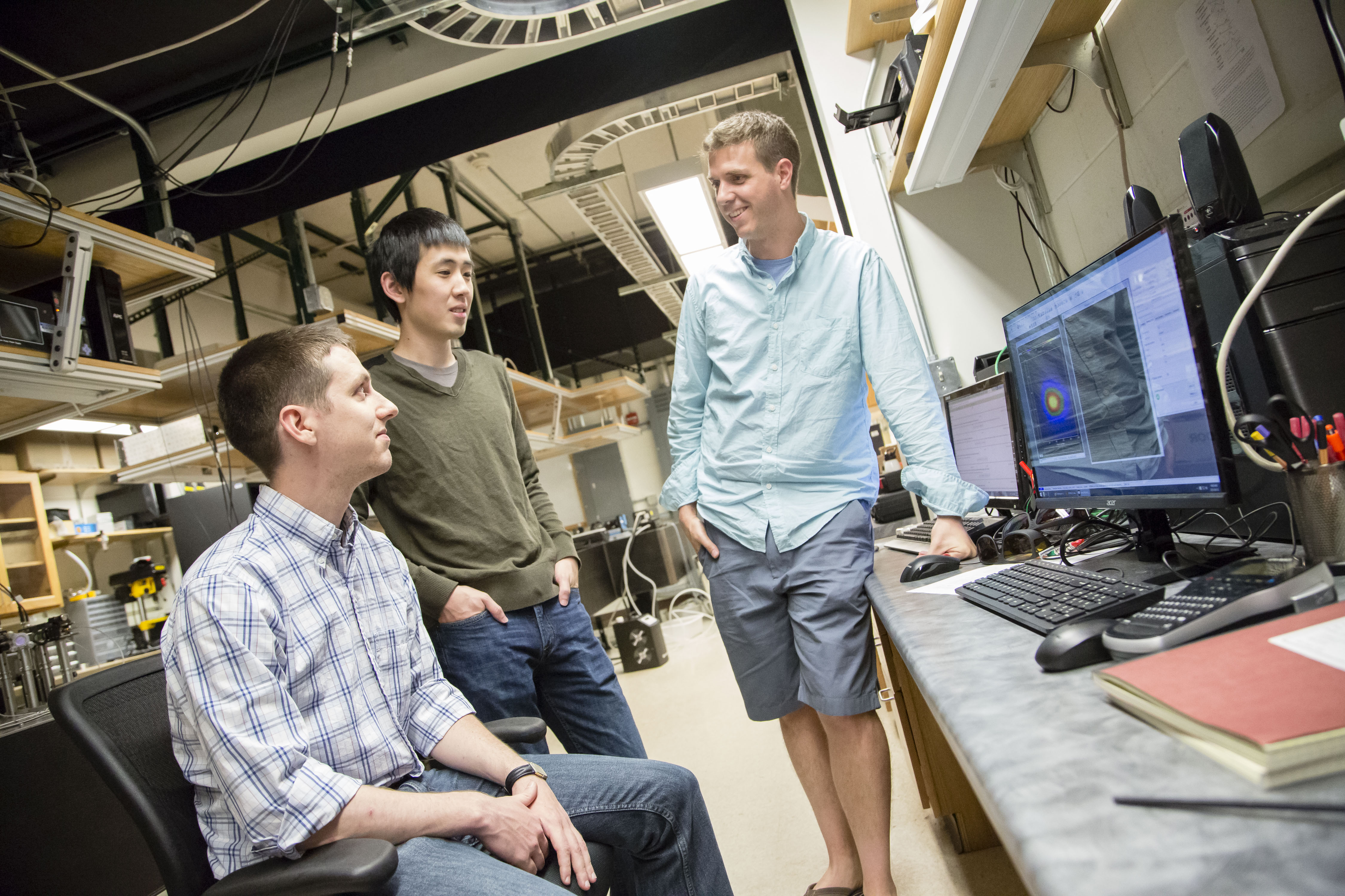 Assistant Professor Bryce Gadway meets with graduate students in his laboratory in the Loomis Laboratory of Physics.