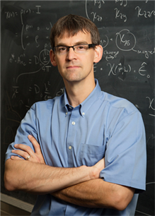 Peter Abbamonte poses in front of blackboard covered in physics formulas