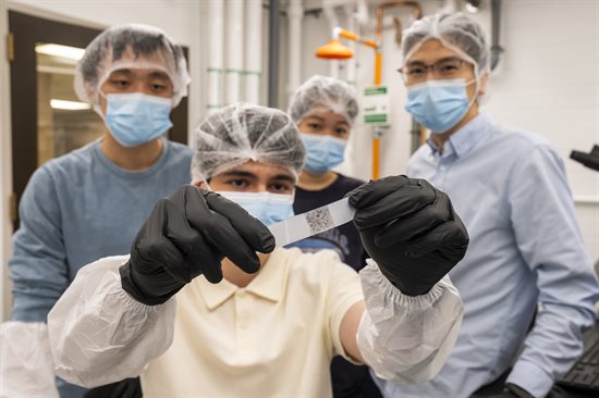 Illinois Physics undergraduate researcher Peter Golemis holds a 2D quantum material adhered to transparent tape. Behind him are fellow student researchers Christopher He (left) and Yimiao &amp;amp;amp;quot;Lilly&amp;amp;amp;quot; Guo (center), and Professor Pengjie Wang, in the Wang laboratory.