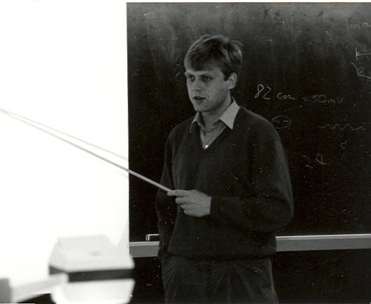 A historical photo of a man with a pointer standing in front of a blackboard.